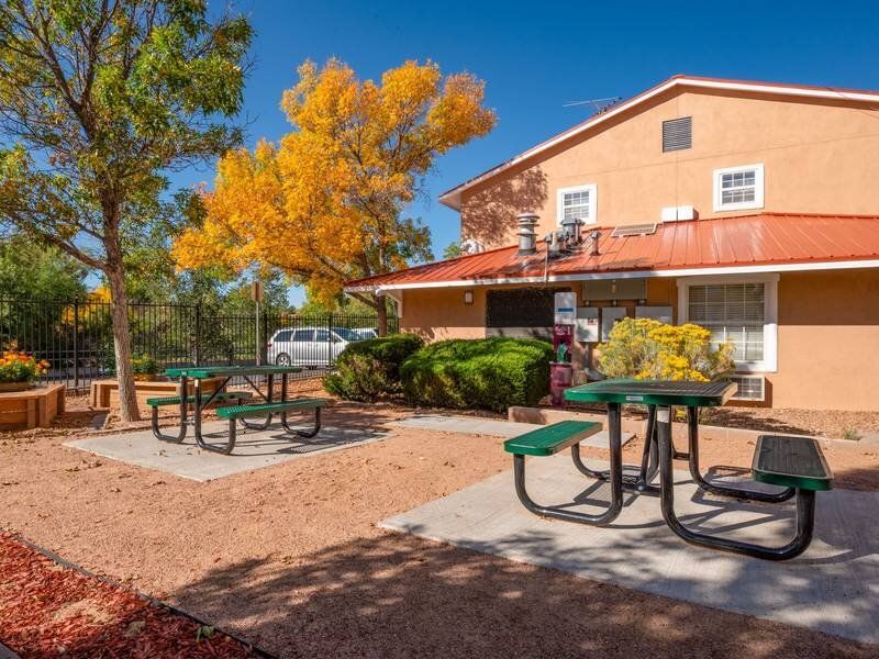 Outdoor community picnic area with green tables beside a peach stucco building at Santa Fe Suites in Santa Fe, NM.
