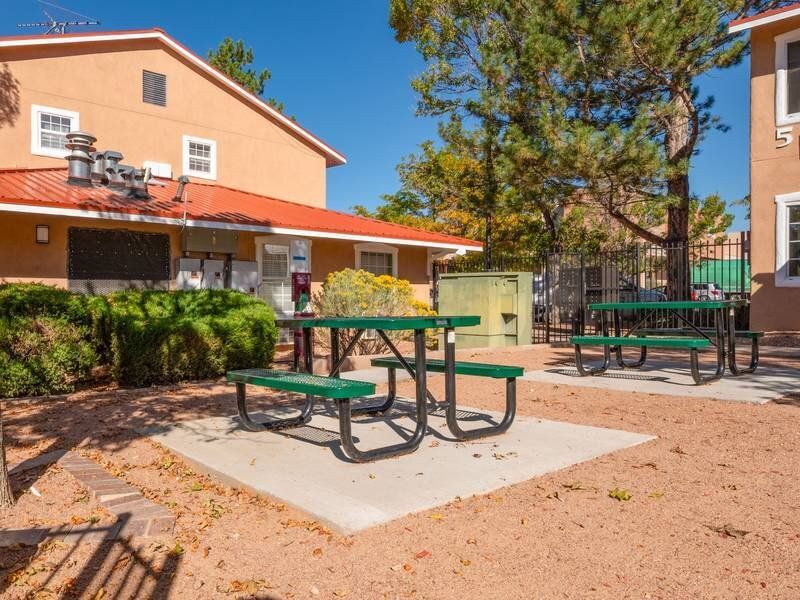 Outdoor communal courtyard with green picnic tables near orange apartment buildings at Santa Fe Suites in Santa Fe, NM.