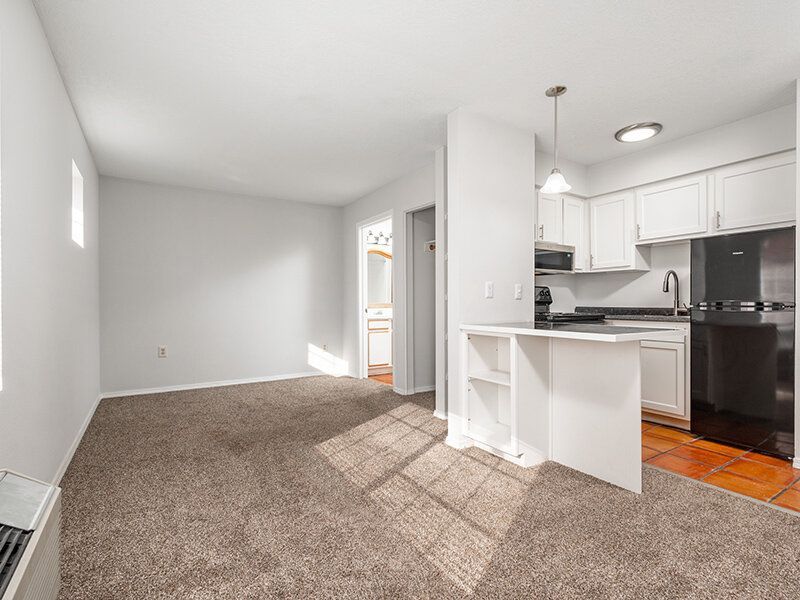 Open living room with carpet, adjacent kitchen, white cabinets, stainless steel fridge, and a breakfast bar at Santa Fe Suites in Santa Fe, NM.