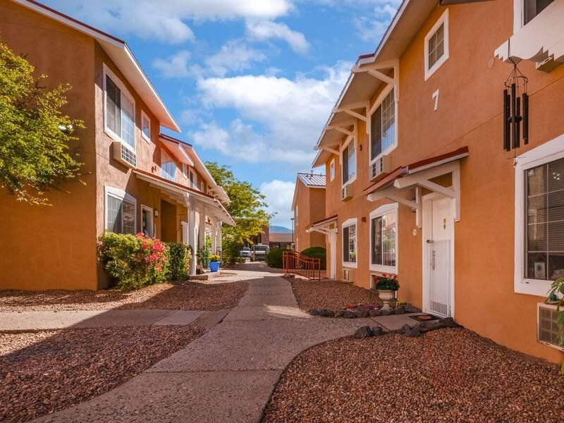 Exterior view of tan two-story apartment buildings with a central walkway at Santa Fe Suites in Santa Fe, NM.