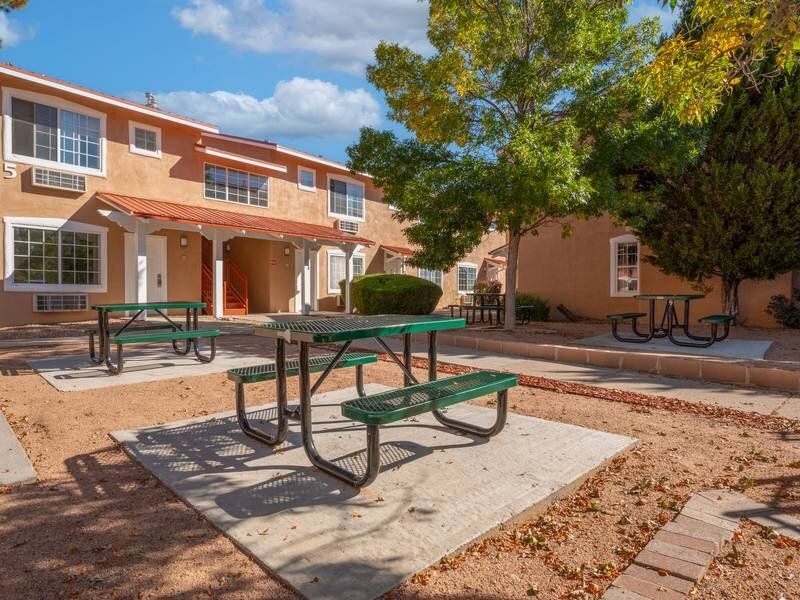 Outdoor courtyard at an apartment complex with green picnic tables and trees at Santa Fe Suites in Santa Fe, NM.