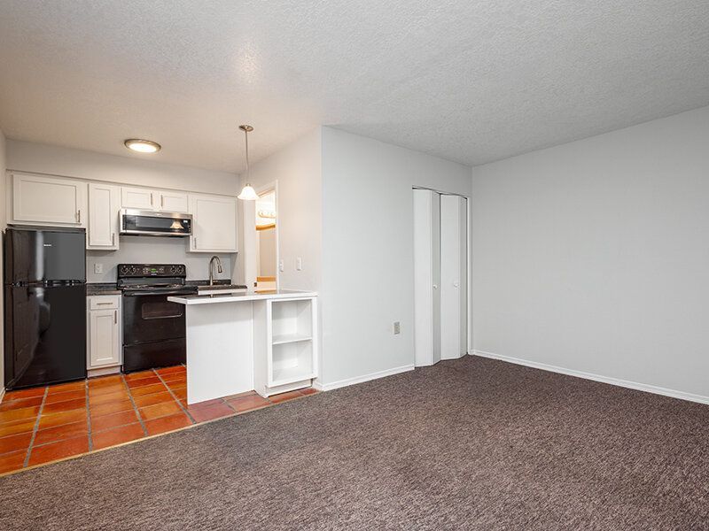 Open-concept apartment living area with a kitchen, black appliances, and tile flooring at Santa Fe Suites in Santa Fe, NM.