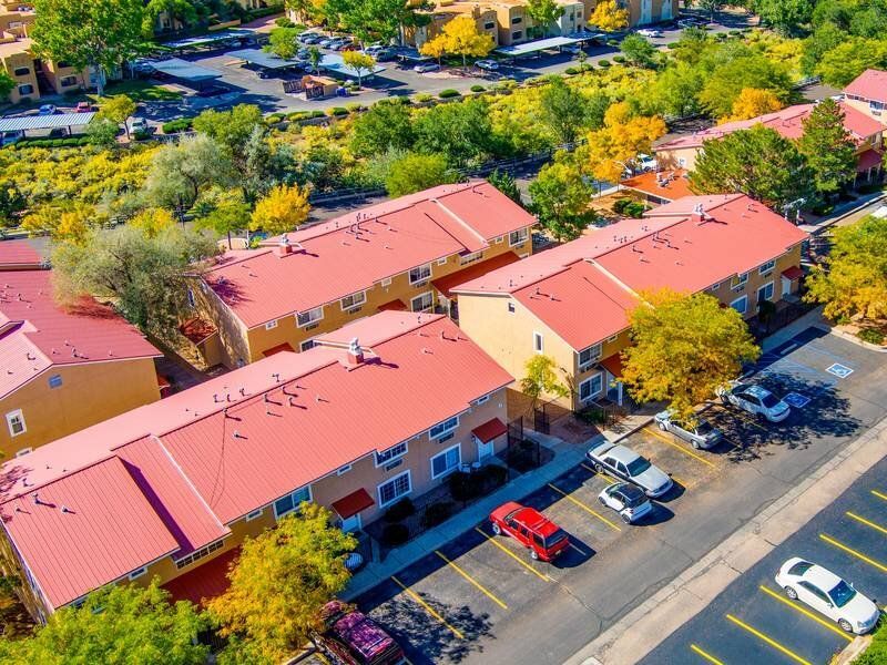 Aerial view of red-roof apartment buildings with parking and trees at Santa Fe Suites in Santa Fe, NM.