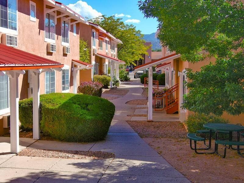 Outdoor courtyard of a multifamily community with walkway, shrubs, and picnic tables at Santa Fe Suites in Santa Fe, NM.