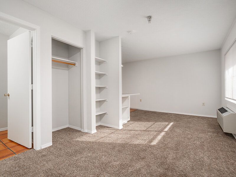 Empty apartment living area with an open closet, built-in shelves, and a window at Santa Fe Suites in Santa Fe, NM.