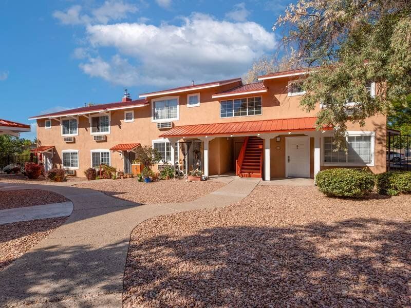 Two-story orange apartment building with red awnings and desert landscaping; curved walkway at Santa Fe Suites in Santa Fe, NM.