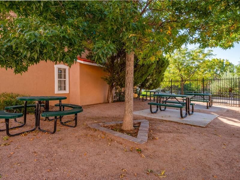 Outdoor community picnic area with green tables, benches, trees, and an orange building at Santa Fe Suites in Santa Fe, NM.