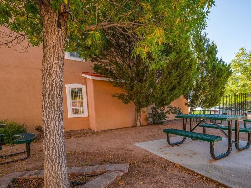 Outdoor apartment community courtyard with trees and a green picnic table at Santa Fe Suites in Santa Fe, NM.