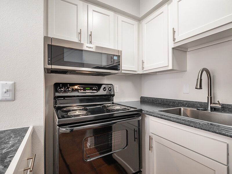 Kitchen with black electric stove, microwave, white cabinets, and a double-basin sink at Santa Fe Suites in Santa Fe, NM.