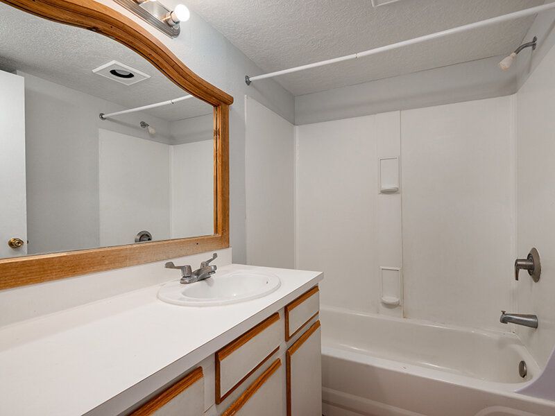 Bathroom with white countertops, sink, wood-framed mirror, and bathtub/shower at Santa Fe Suites in Santa Fe, NM.