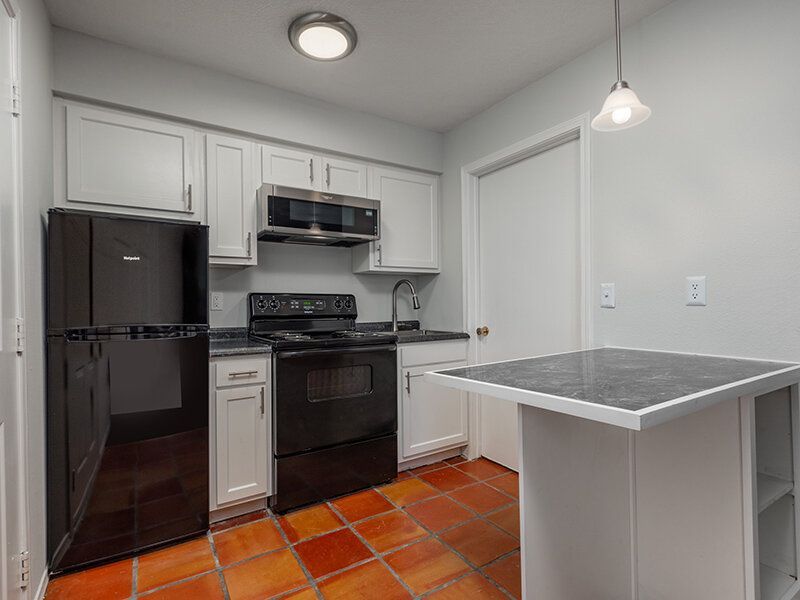 Kitchen with white cabinets, black fridge, stove, microwave, and a small island on terracotta tile floor at Santa Fe Suites in Santa Fe, NM.