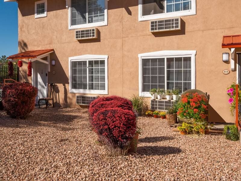 Exterior view of a brown stucco apartment building with a gravel yard and potted plants at Santa Fe Suites in Santa Fe, NM.