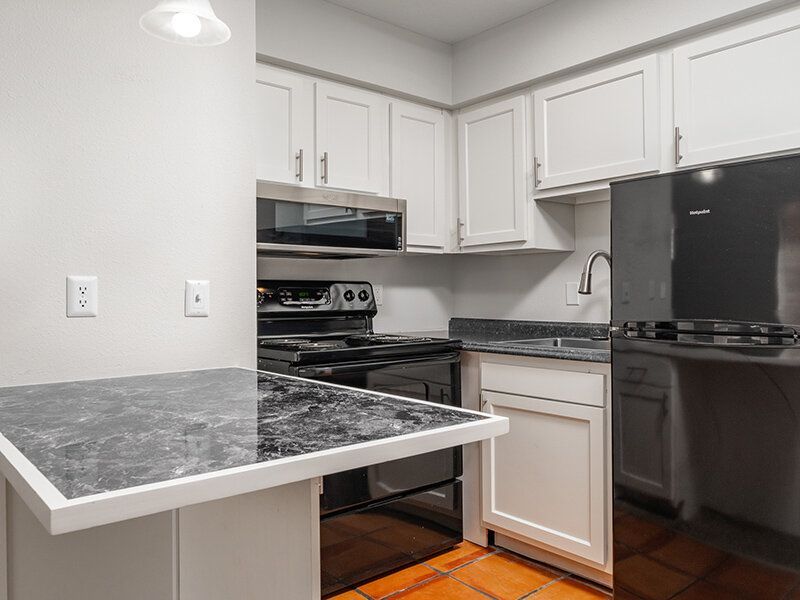 Kitchen in an apartment with white cabinets, black appliances, and granite countertops at Santa Fe Suites in Santa Fe, NM.