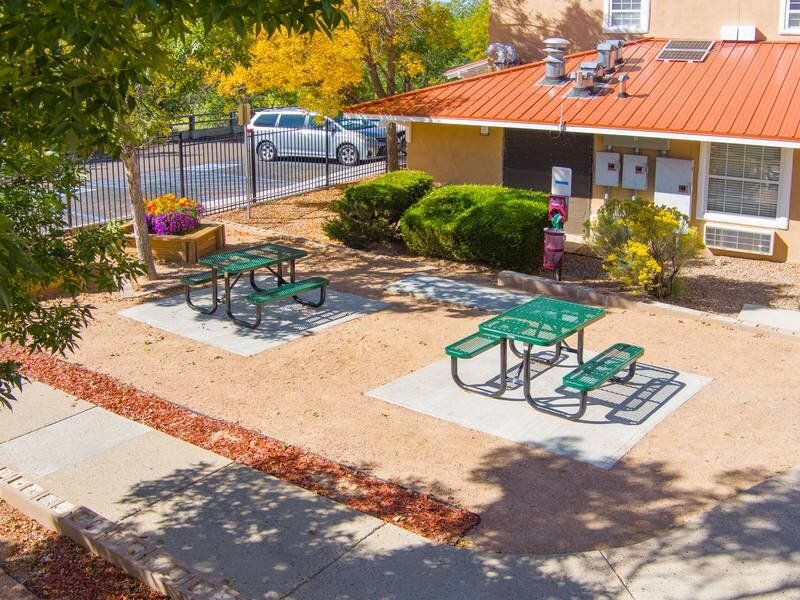 Outdoor communal area with green picnic tables beside a building at Santa Fe Suites in Santa Fe, NM.