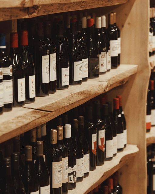 Several bottles of wine are lined up on a wooden shelf