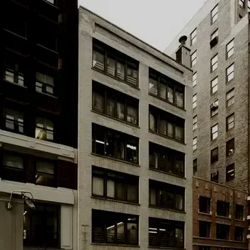 A large building with a lot of windows is surrounded by smaller buildings.