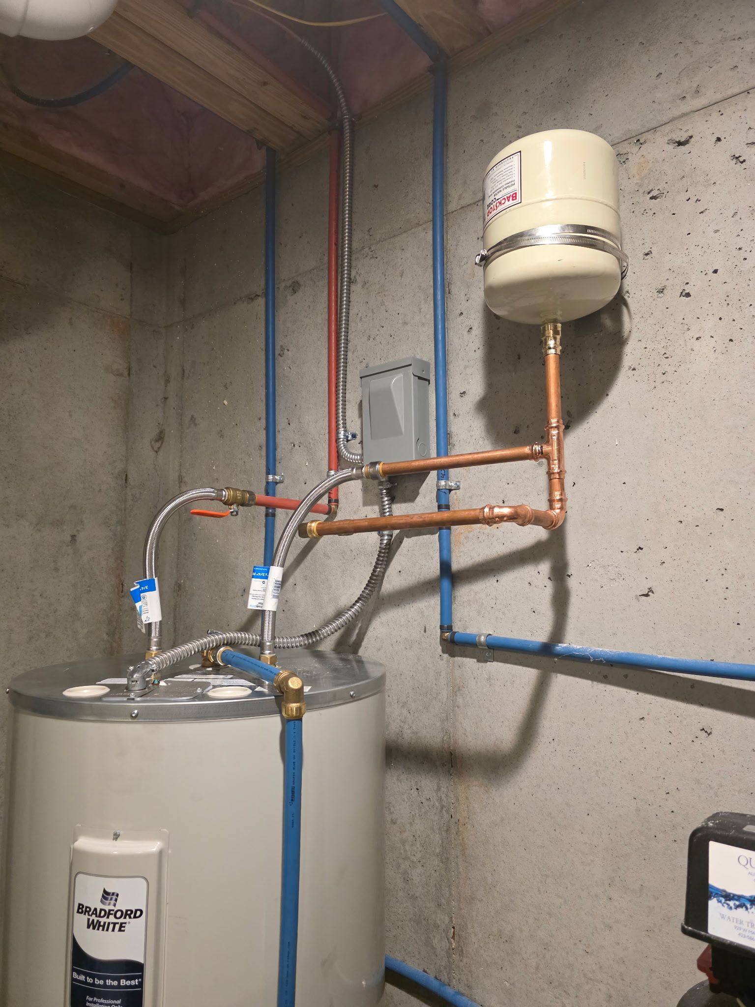 Water heater with blue pipes and expansion tank in a basement setting.
