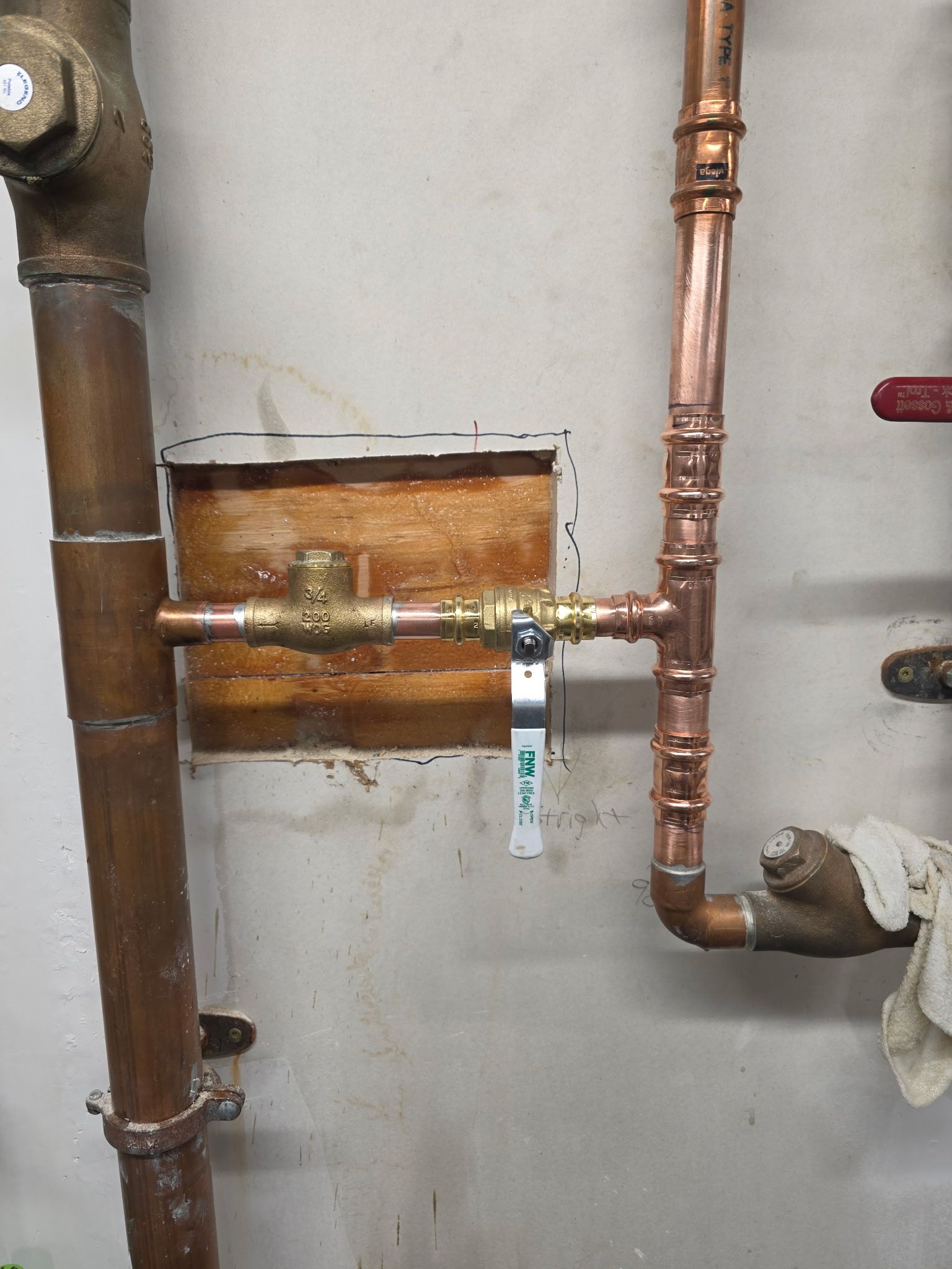Copper pipes and valve on a wall, connected to other pipes.