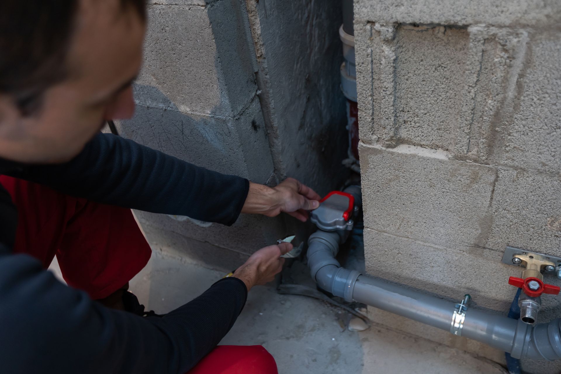 A man repairs a pipe inside a wall, using tools and focused on the task at hand.