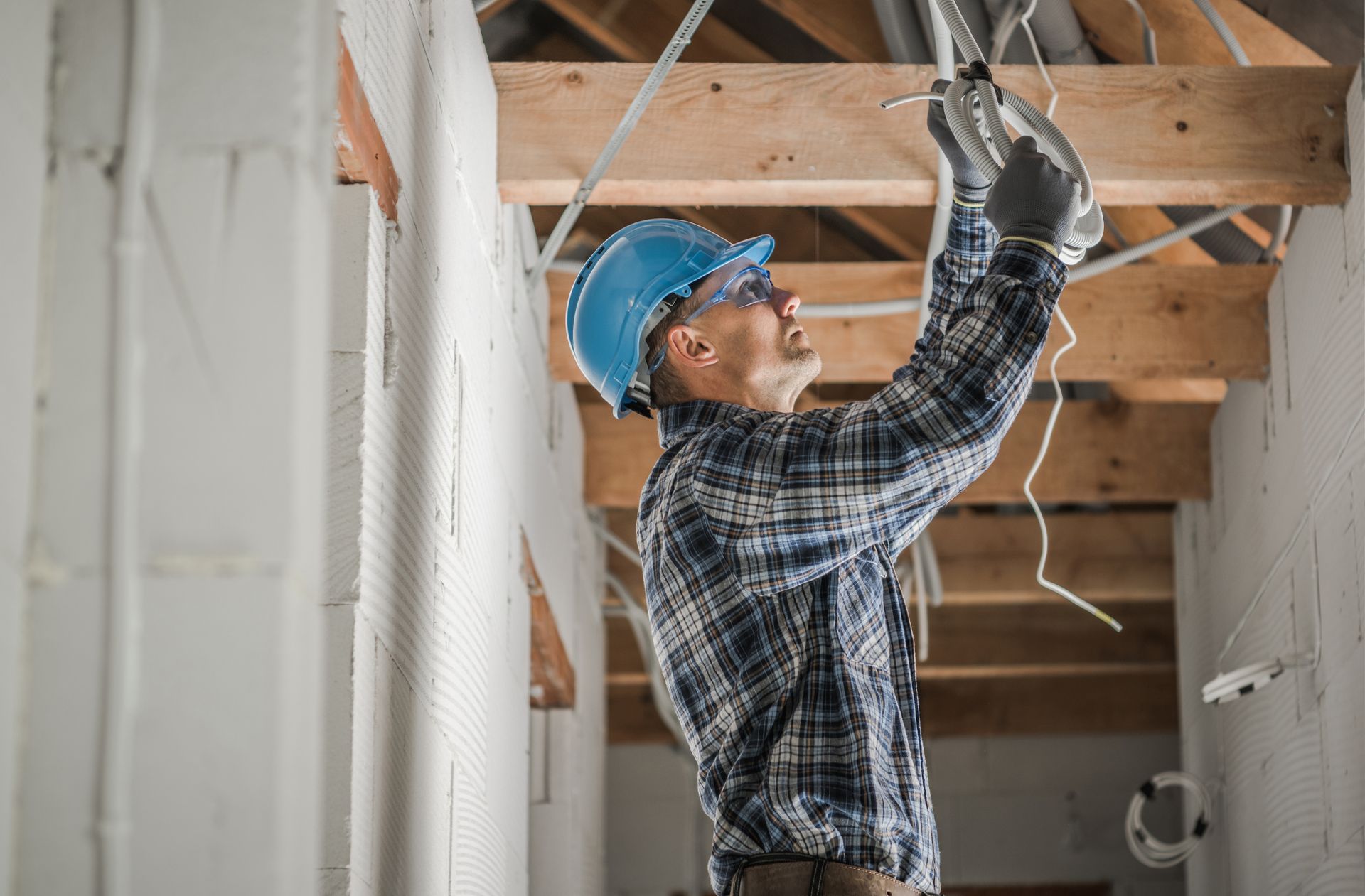 Plumber repairing kitchen sink plumbing while homeowner stands nearby in the background.
