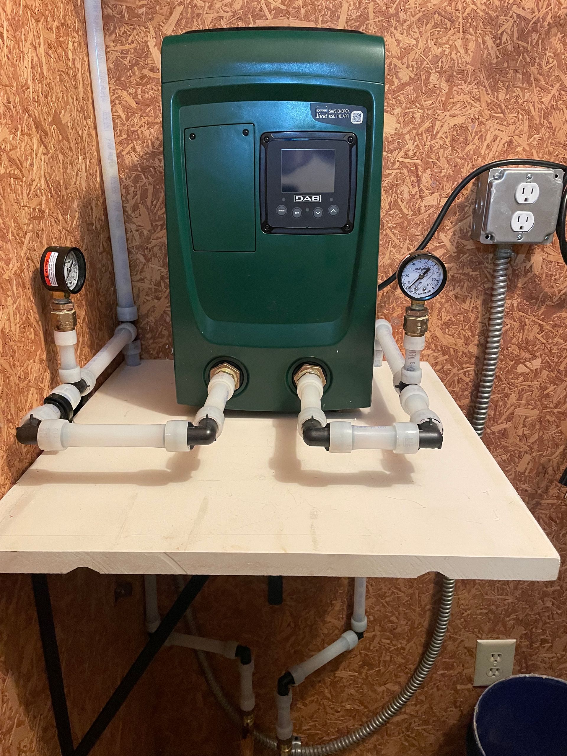 Green water pump system with gauges and pipes, mounted on a white tabletop in a utility room.