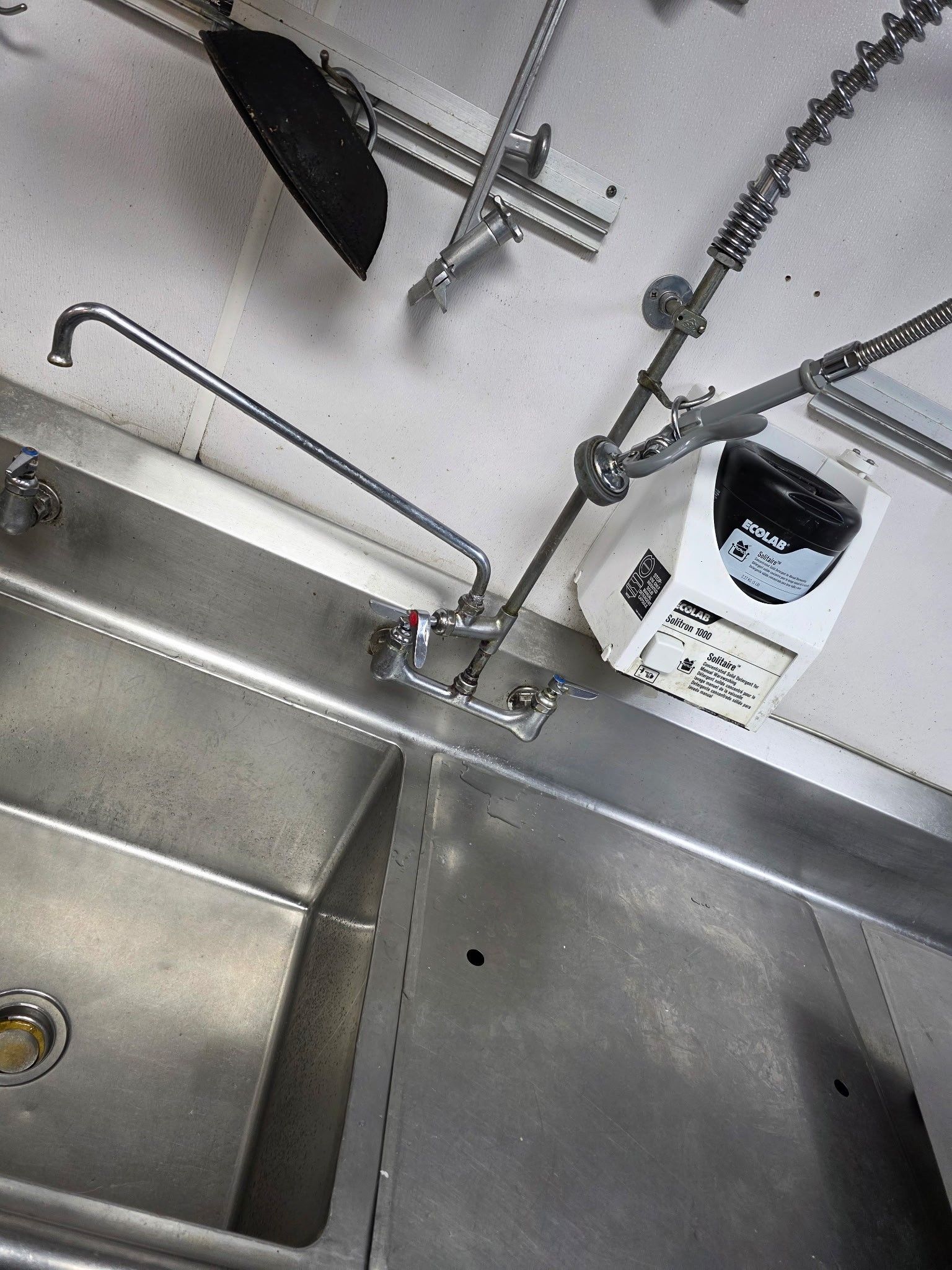 Stainless steel kitchen sink with faucet and sprayer, likely in a commercial setting.