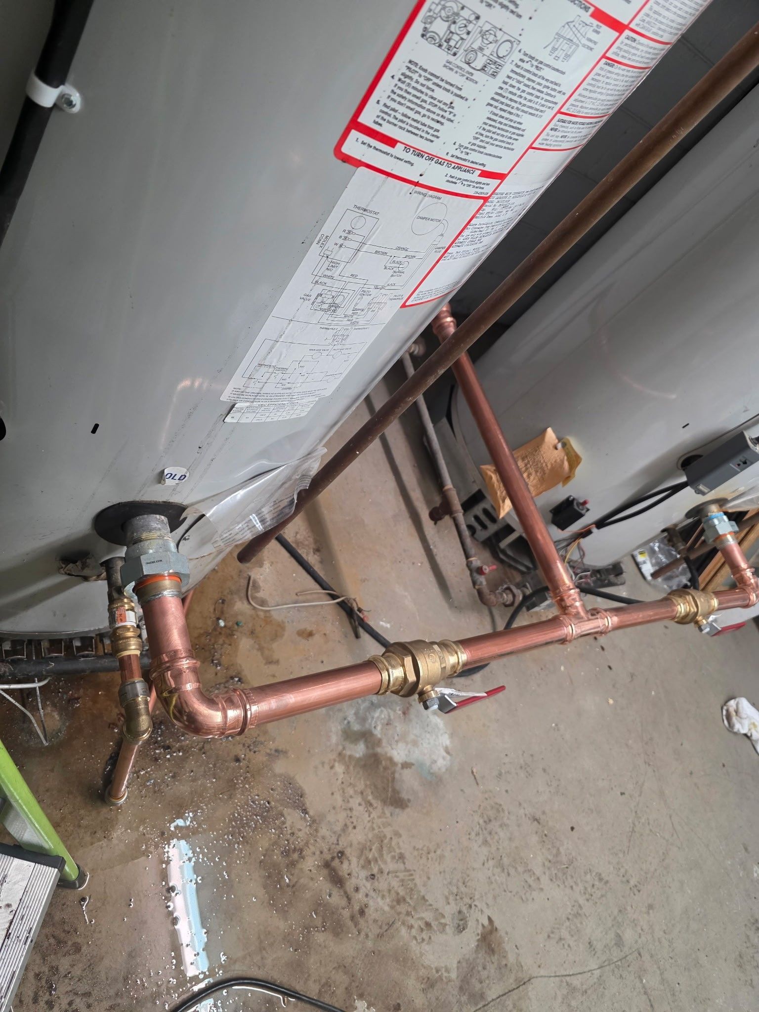 Copper pipes connecting to a hot water tank in a garage. Water on the floor.