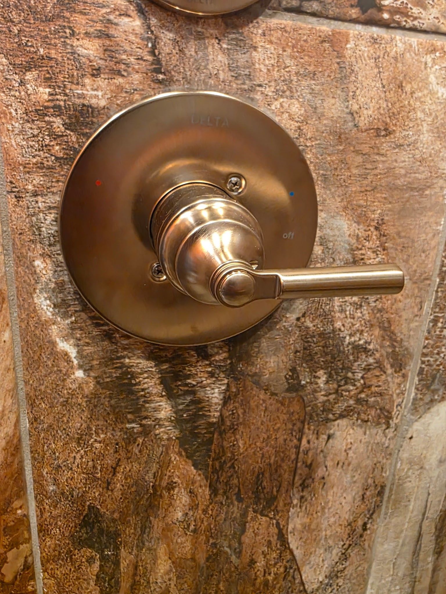 Bronze shower faucet handle on a patterned, brown tiled wall.