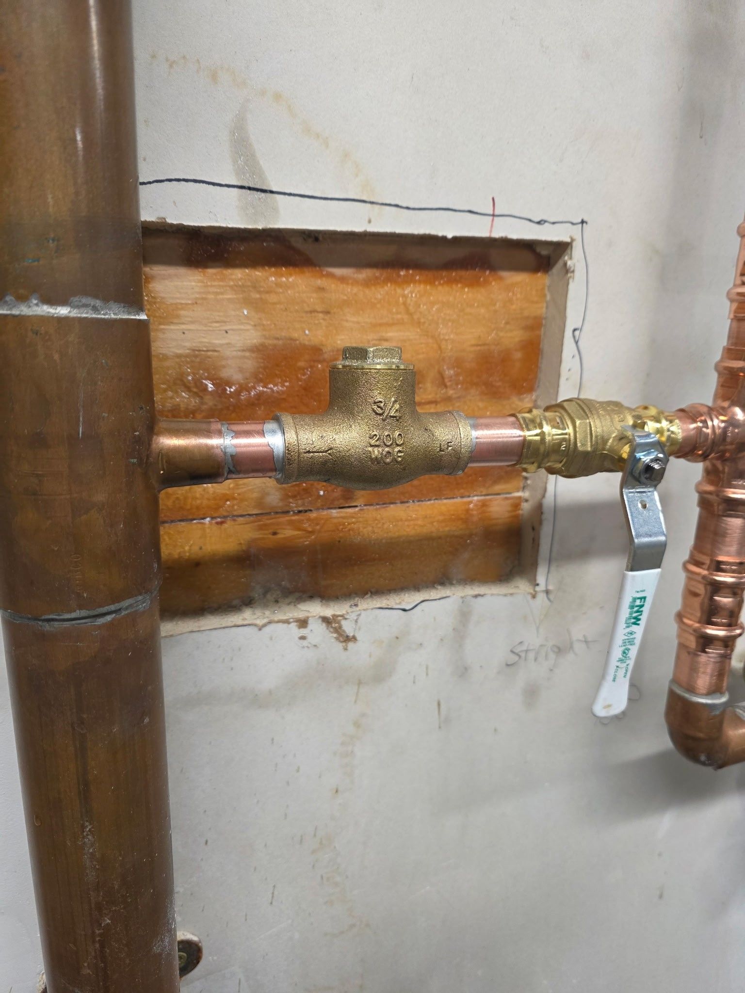Plumbing pipes with a valve and ball valve, against a wall with a wooden patch.