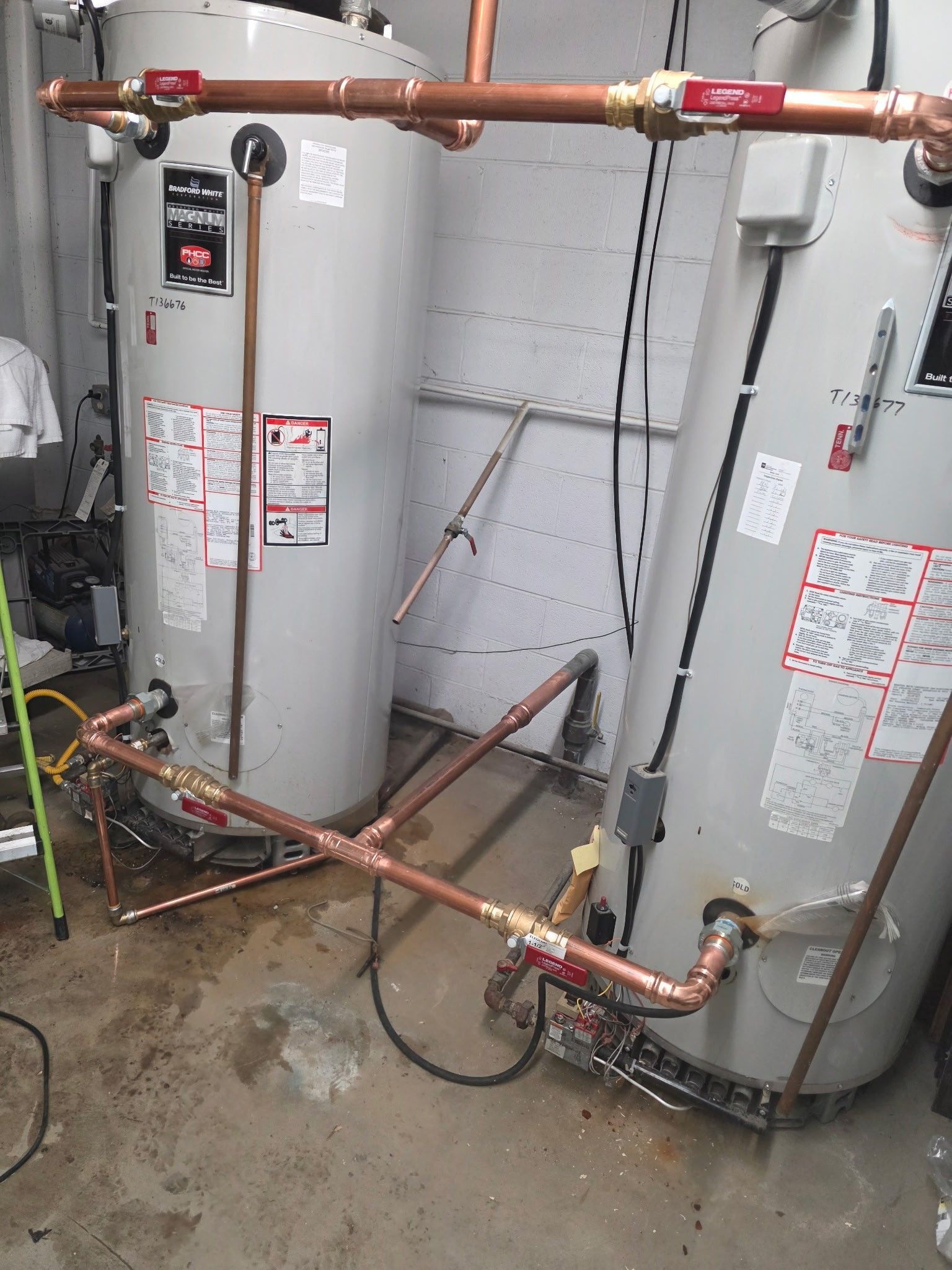 Two water heaters with copper pipes and red valve handles in a utility room.