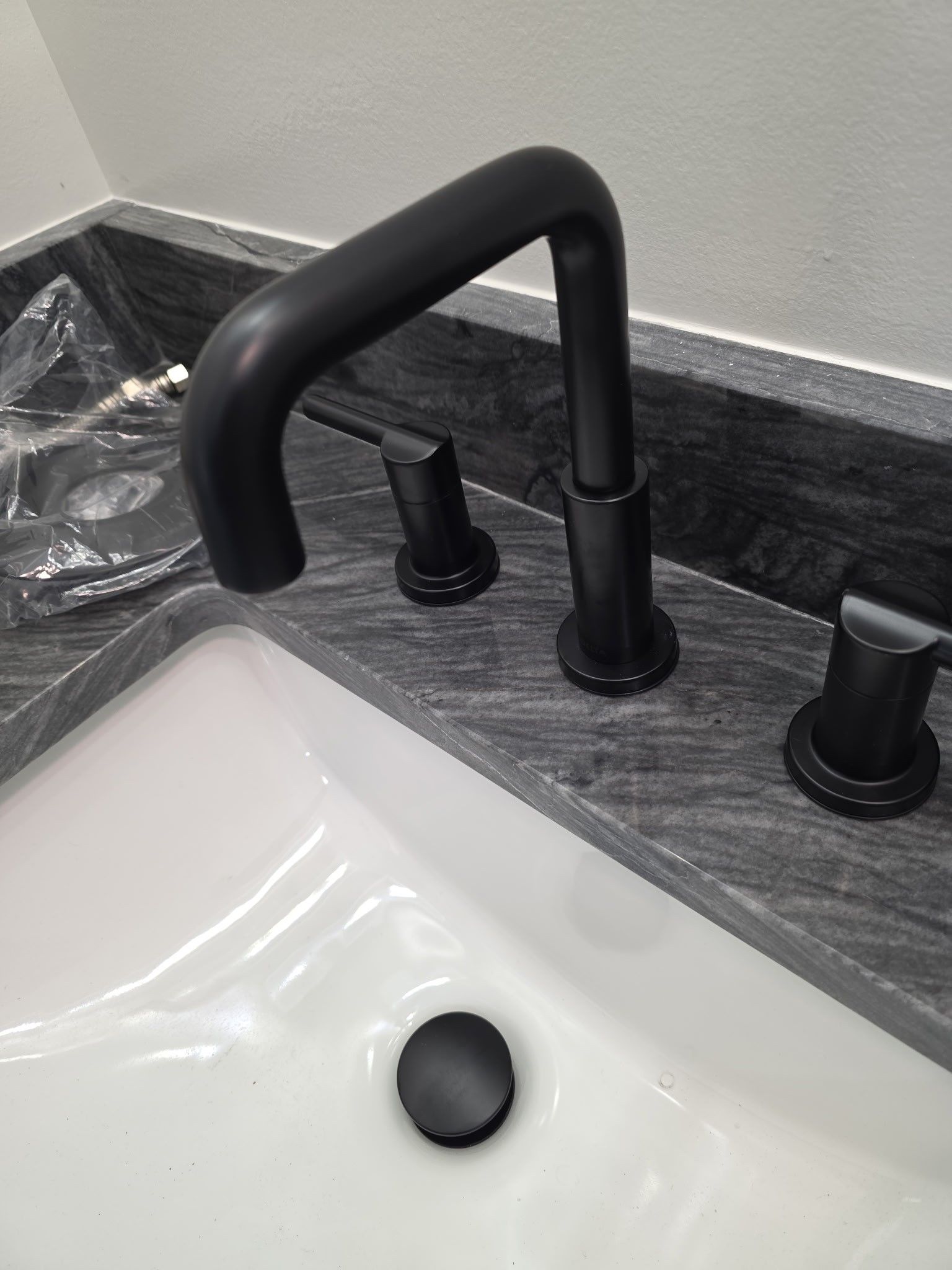 Black faucet and handles on a dark granite countertop above a white sink.