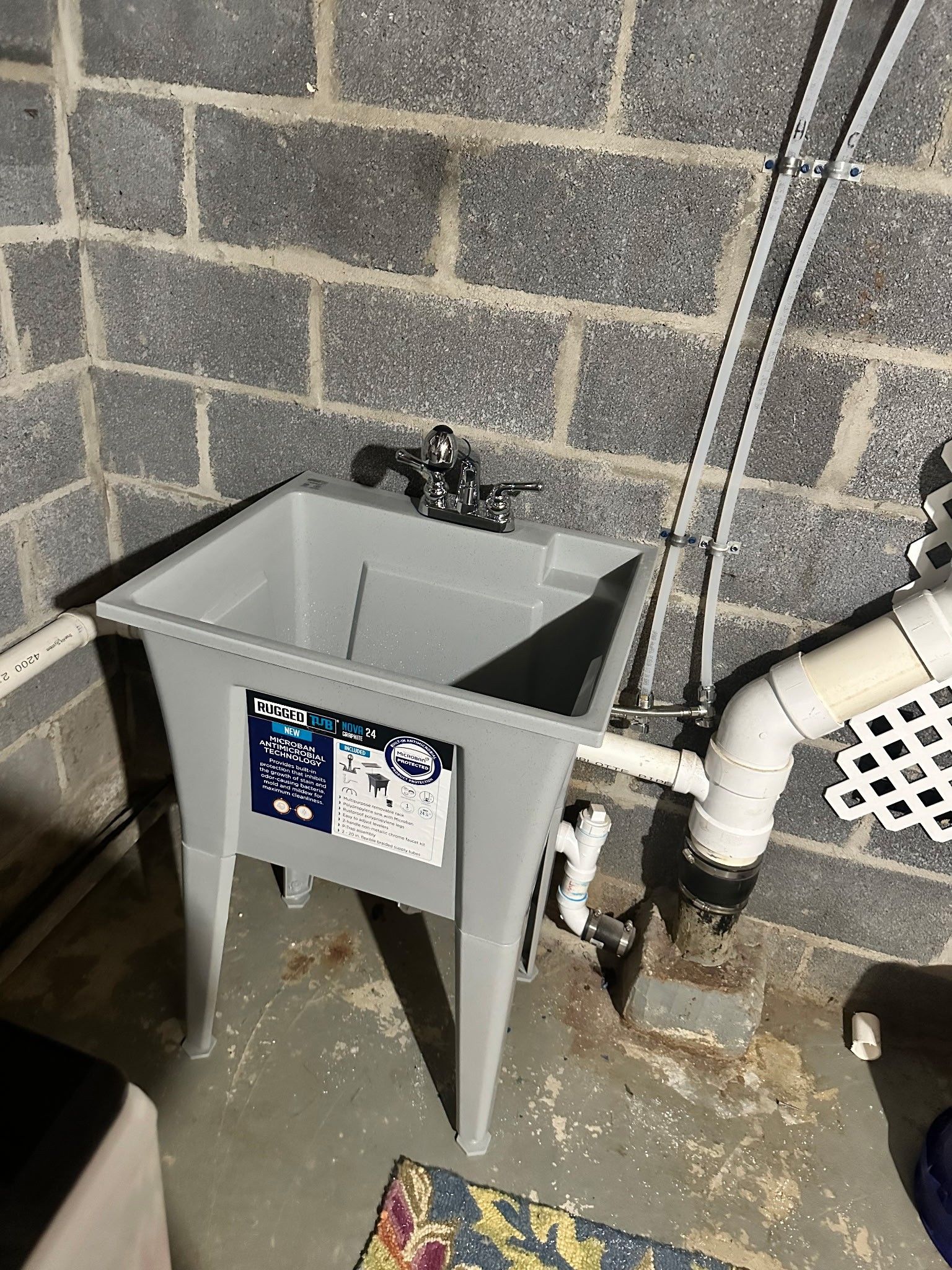 Gray utility sink in a basement, with faucet, pipes, and concrete block wall.