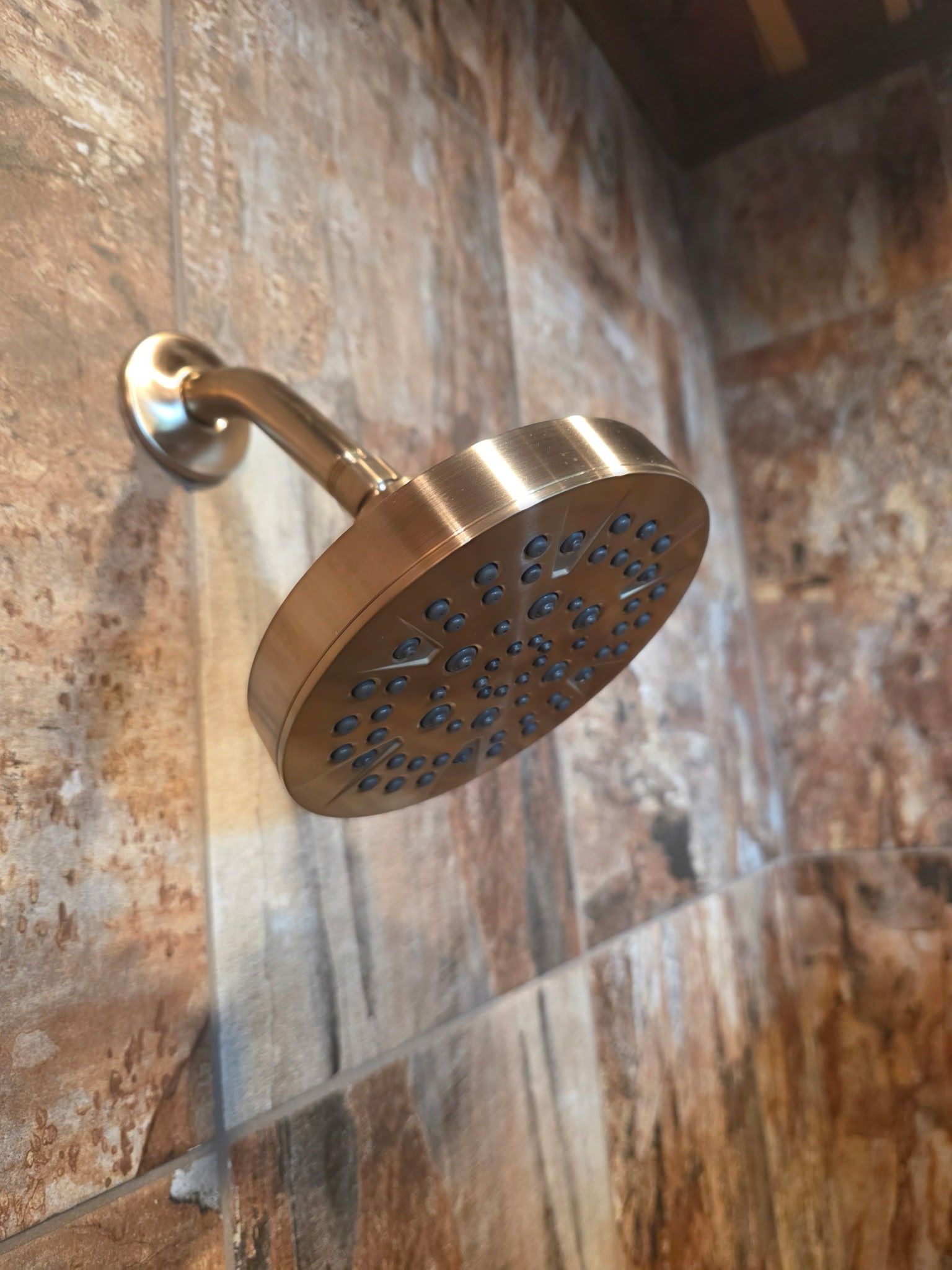 Brass shower head on a textured, brown tiled wall.