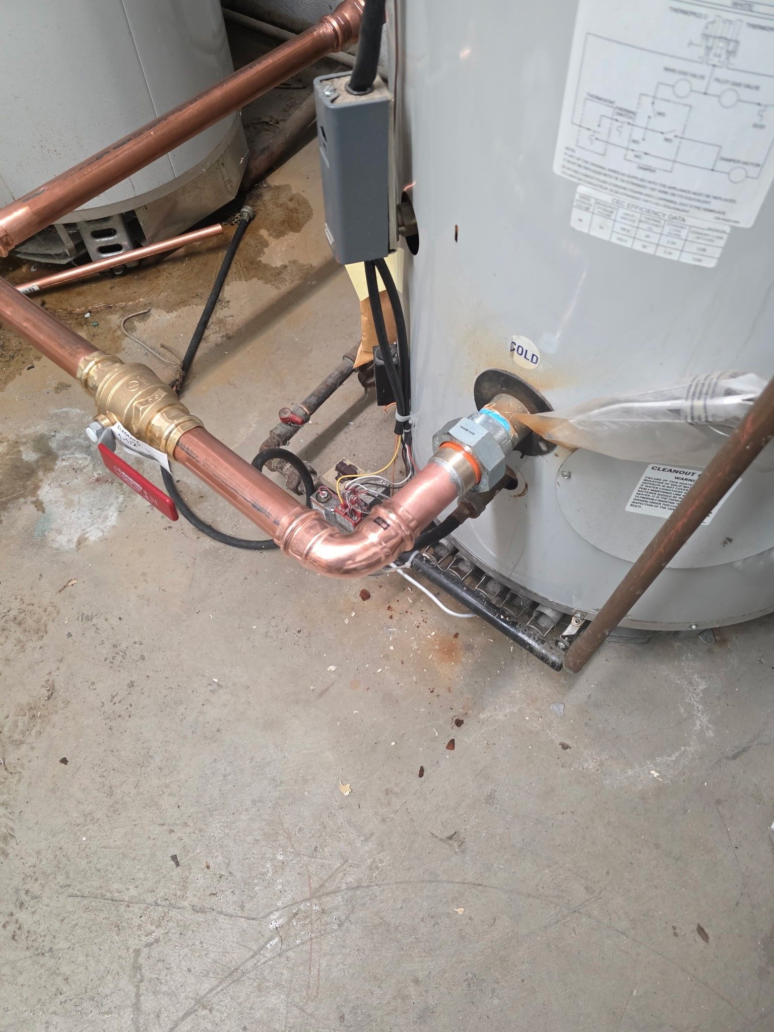Copper pipes connected to a water heater in a concrete-floored room.
