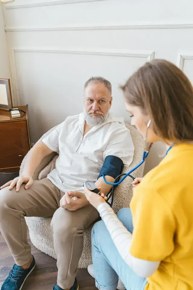 Health worker checking blood pressure of a seated patient in a home setting