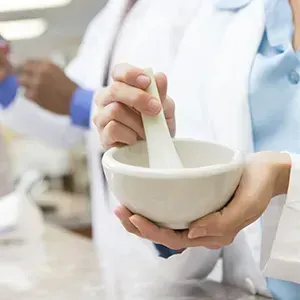 Person using a mortar and pestle in a bright lab, with test tubes in the background