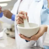 Person using a mortar and pestle in a bright lab, with test tubes in the background