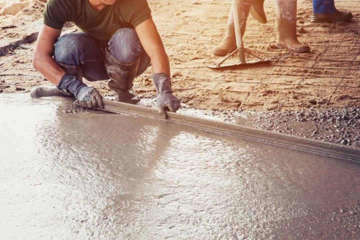 Worker smoothing wet concrete with a trowel at a construction site