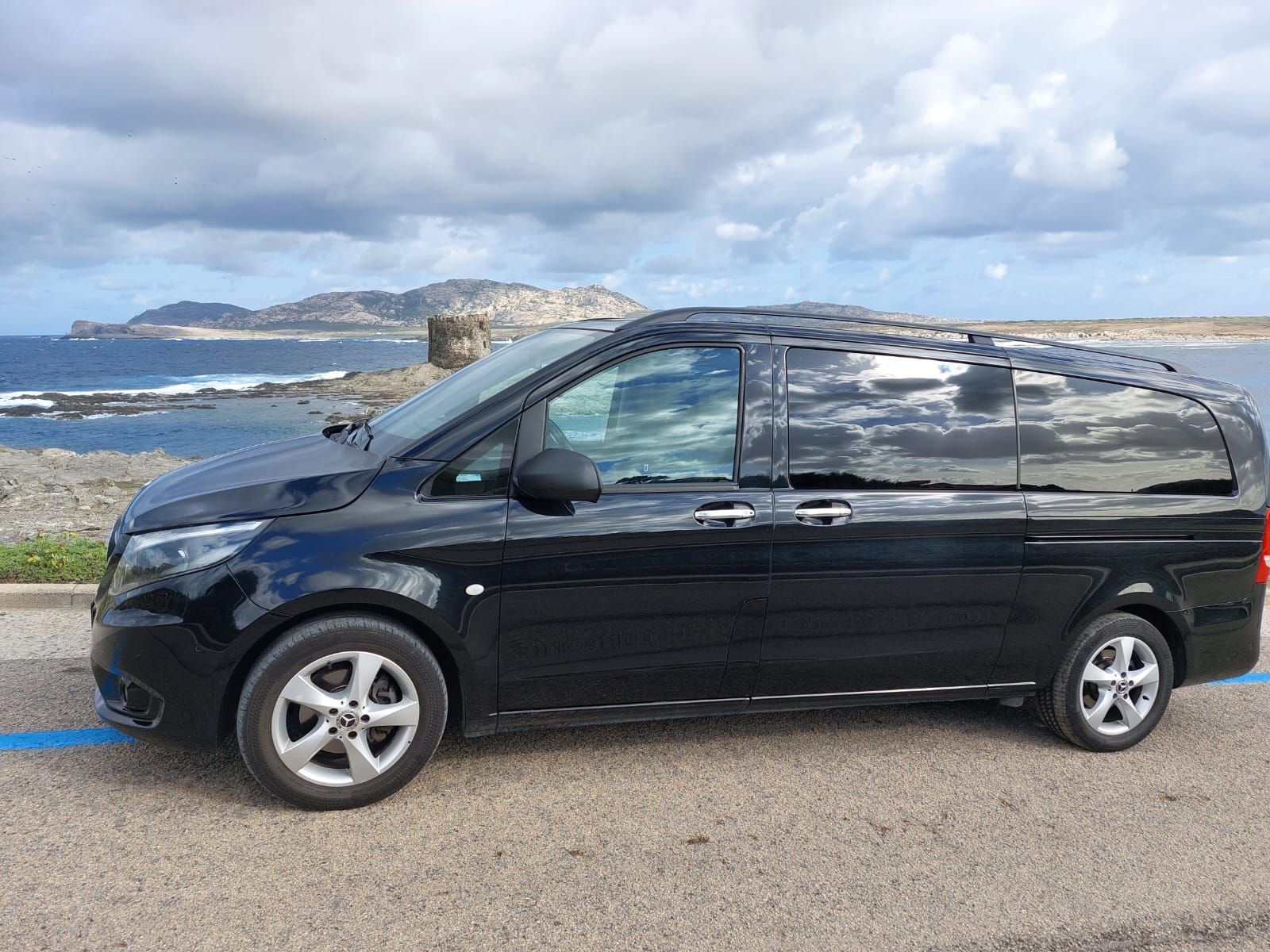 una minivan nera è parcheggiata in un parcheggio vicino all'oceano