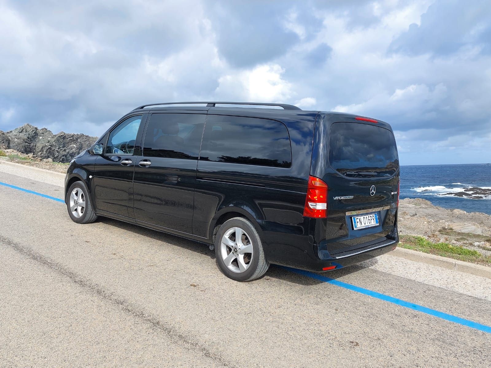 un furgone nero mercedes benz è parcheggiato su una strada accanto al mare