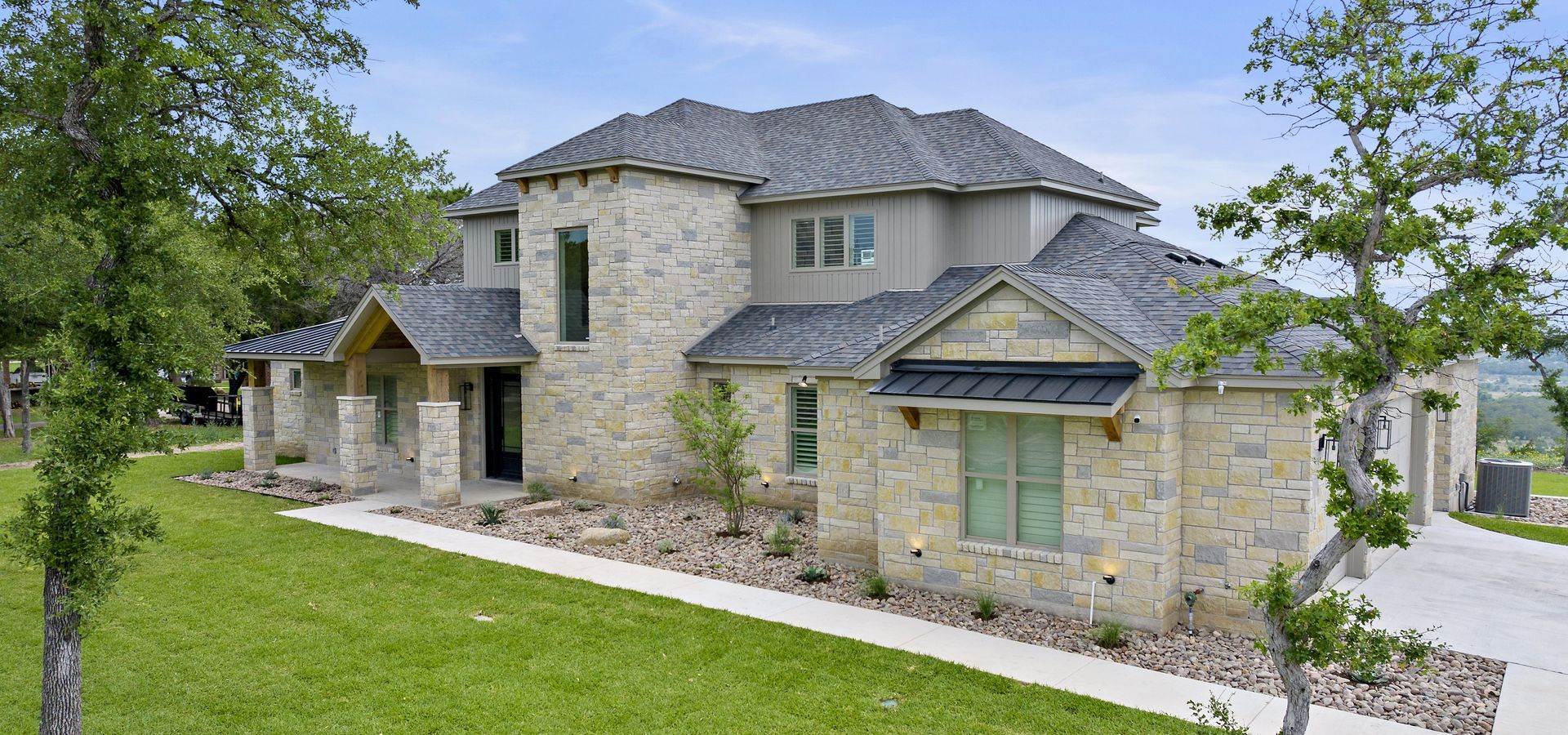Stone two-story house with gray roof and green lawn, viewed from the front corner.