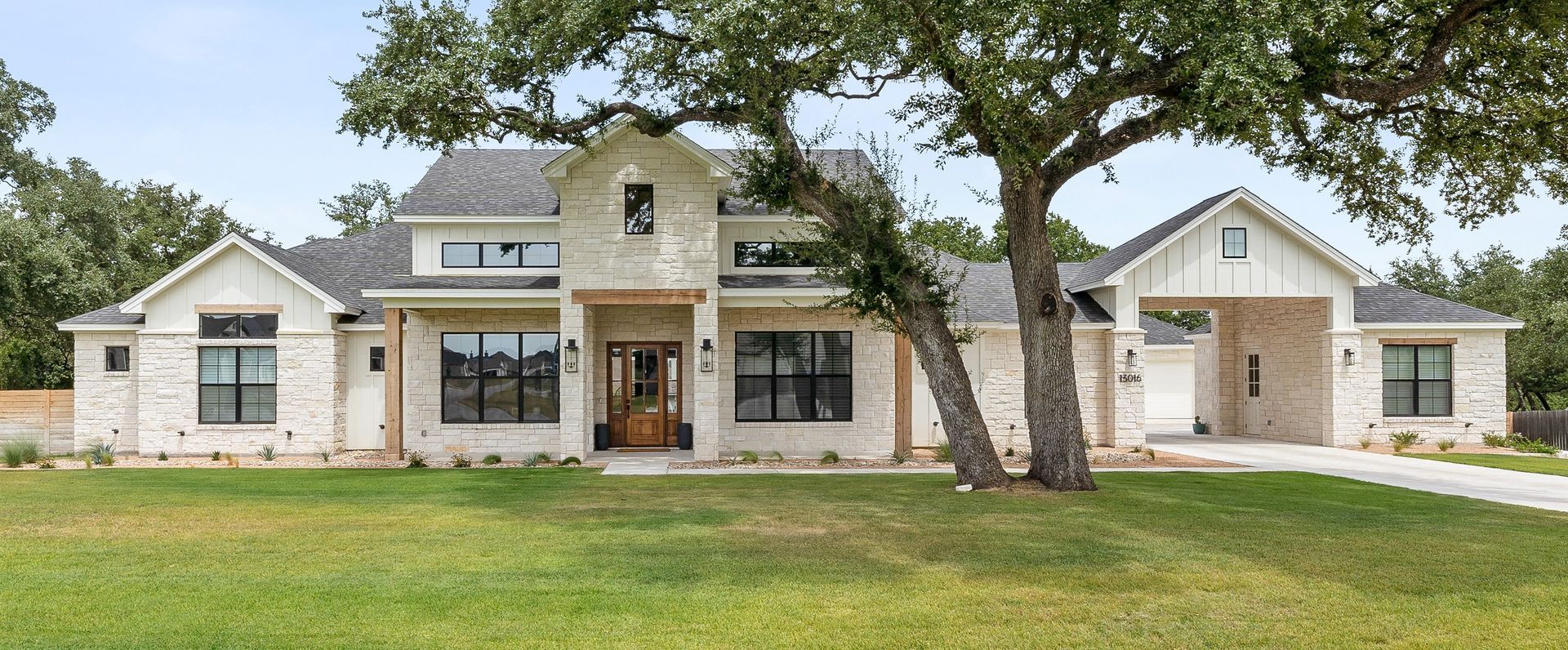 Front view of a modern stone house with large windows, a central entryway, and a green lawn in front