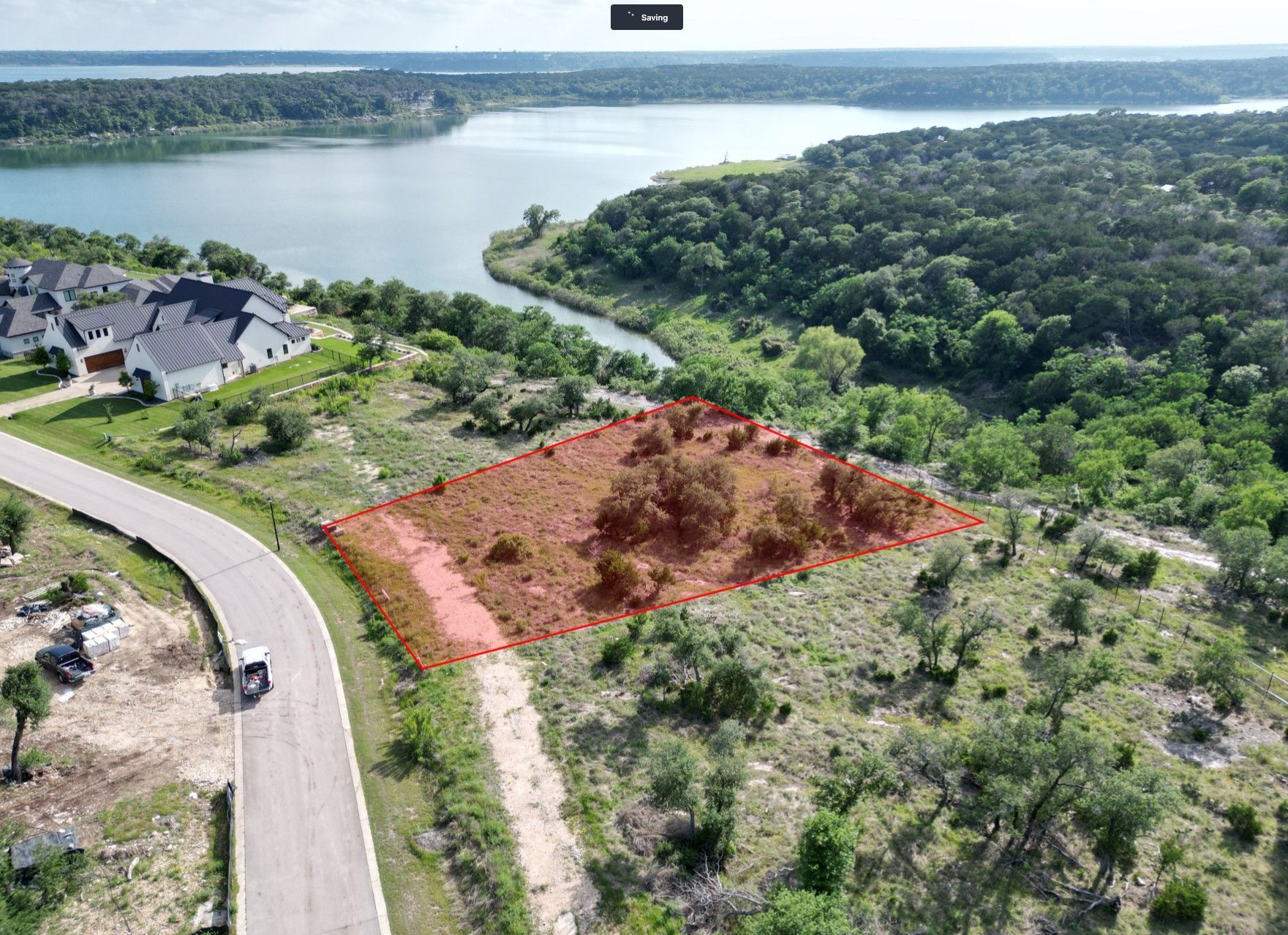 Aerial view of a lakeside lot with a red-marked clearing beside a winding road and forested shoreline.