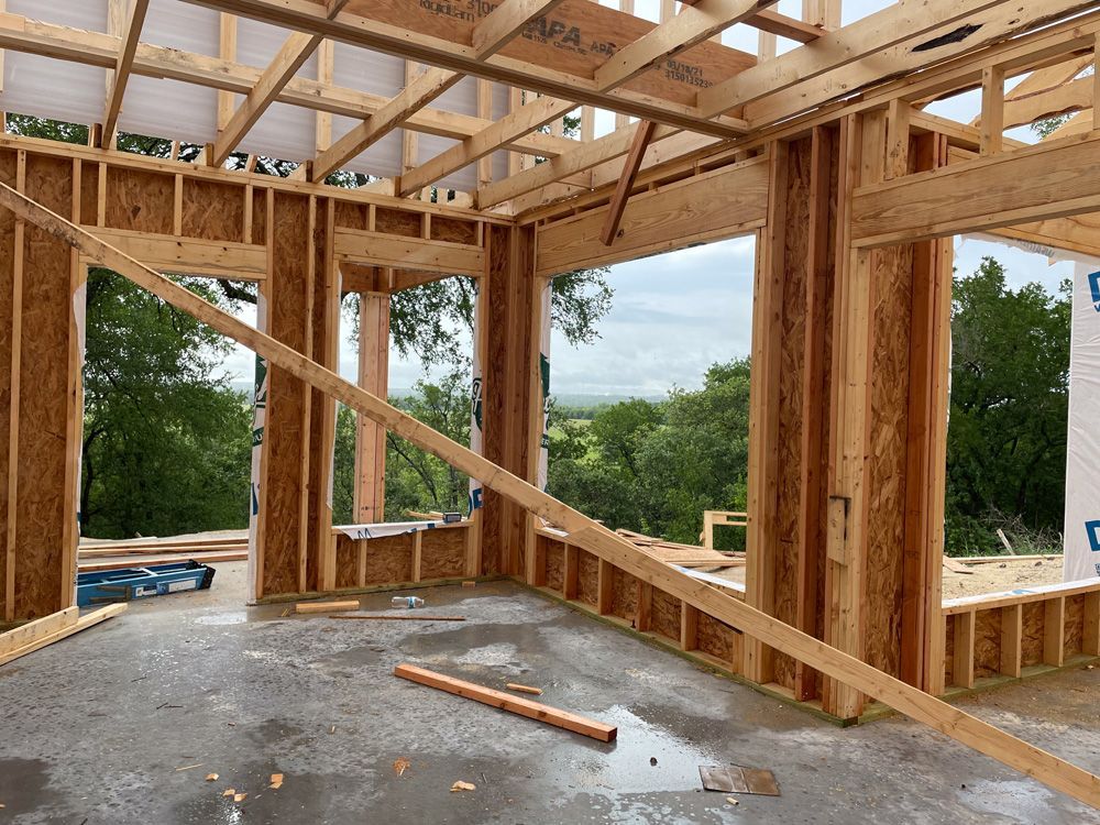 Wood-framed house interior under construction with exposed beams and unfinished concrete floor