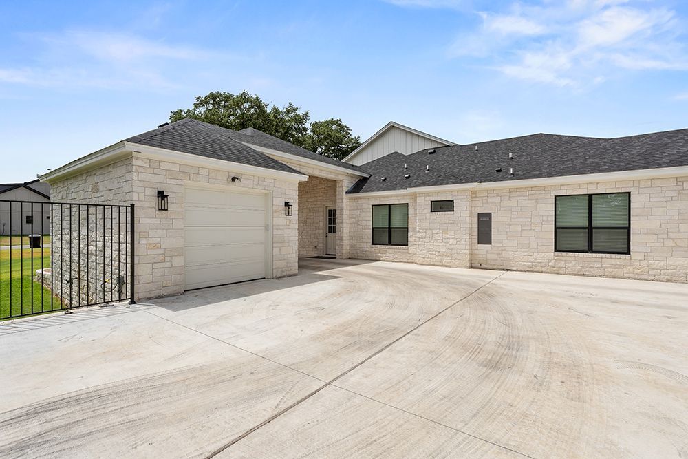 Light brick house exterior with wide concrete driveway and black metal gate