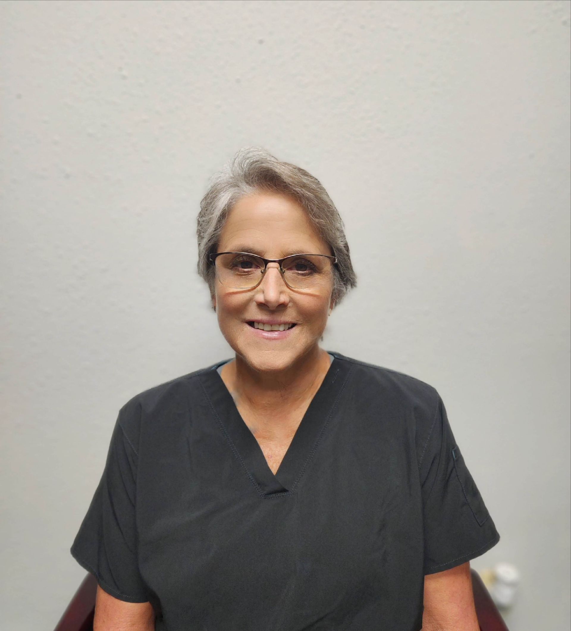 A woman wearing glasses and a black scrub top is smiling for the camera.