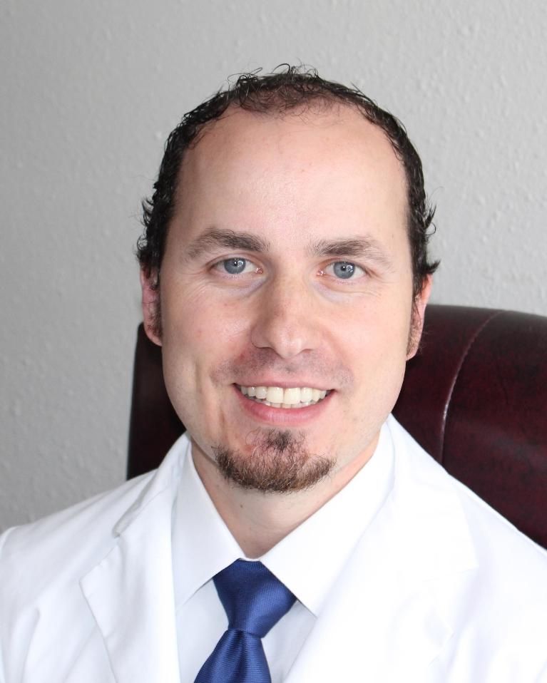 A man in a white coat and blue tie smiles for the camera