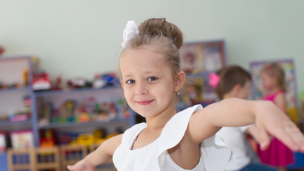A little girl in a white dress is dancing in a classroom.