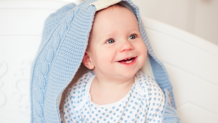 A baby is wrapped in a blue blanket and smiling.