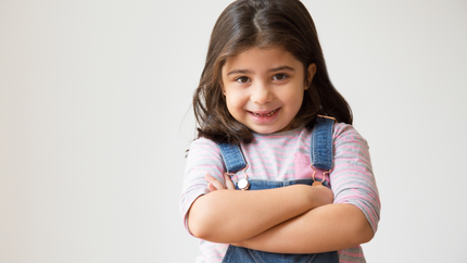 A little girl is standing with her arms crossed and smiling.